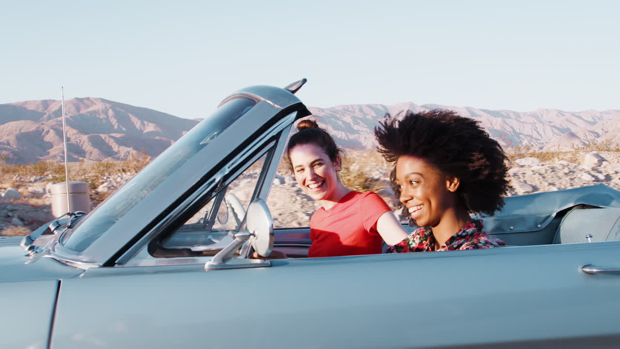 dos amigas conduciendo un coche abierto en una carretera del desierto