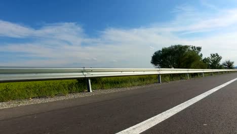 sport pov driving on rural road with metal shield fence beside the field on a sunny day