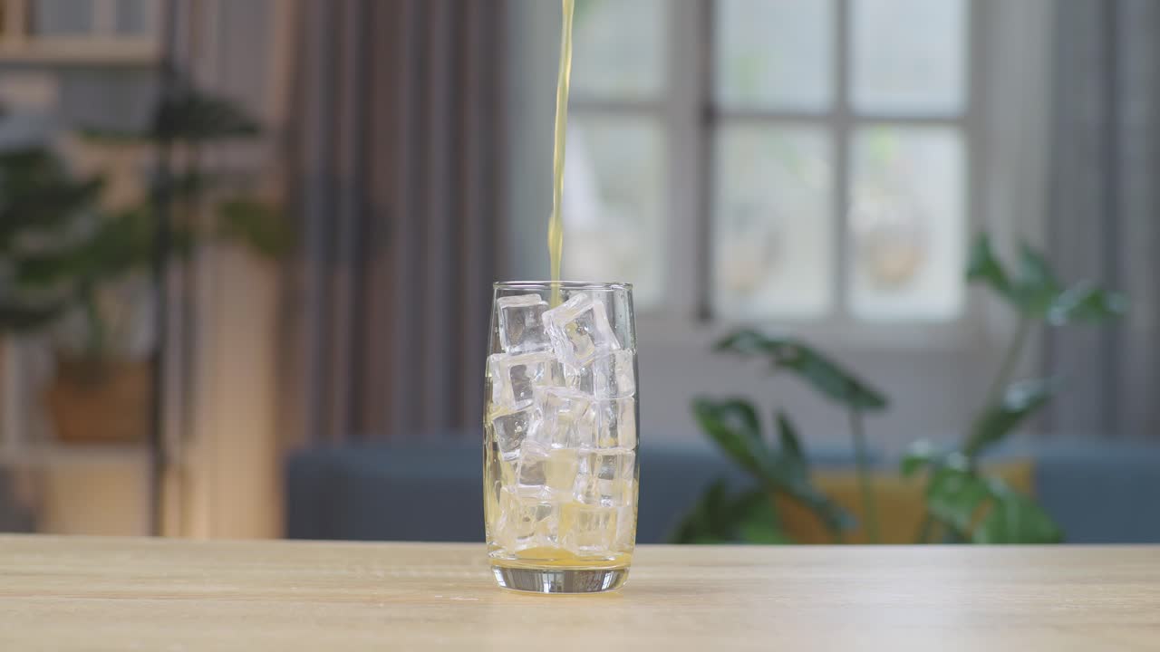 오렌지 주스가 집에서 테이블에 얼음 큐브와 함께 유리잔에 부어지고 있습니다.