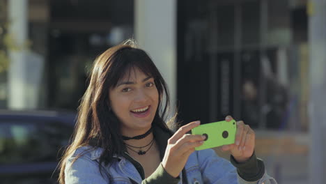 Mujer-Joven-Sonriente-Sosteniendo-Un-Teléfono-Inteligente-Verde-Al-Aire-Libre.