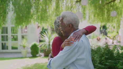 Loving-Senior-Couple-Standing-In-Garden-At-Home-And-Hugging-After-Retirement