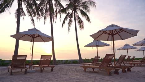 empty beds and sunshades by sandy beachfront of luxury tropical resort on sunset sunlight, static view