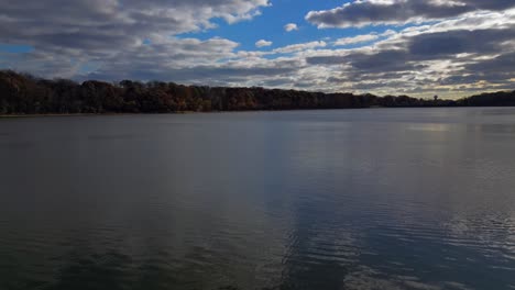 A-low-angle-view-over-a-peaceful-lake,-just-before-a-cloudy-sunset