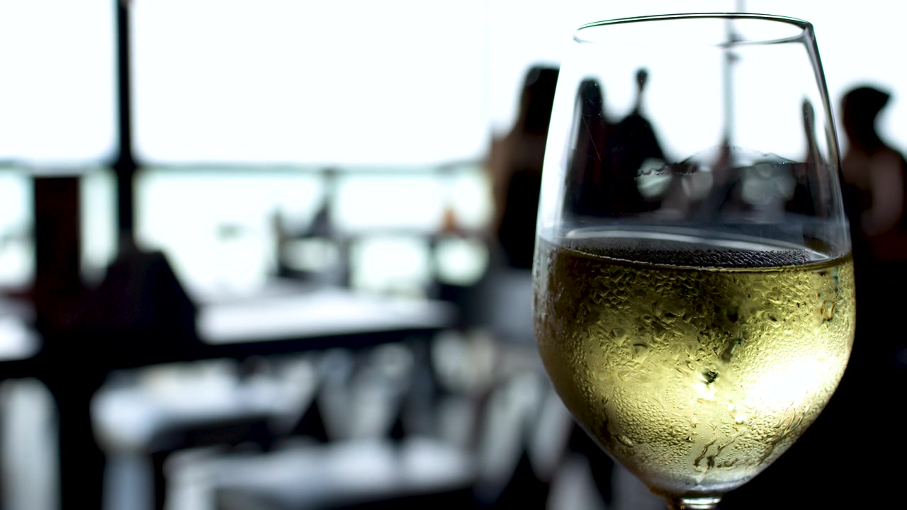 Primo piano di un bicchiere di vino bianco coperto di condensa in un luminoso ristorante all'aperto in Thailandia.