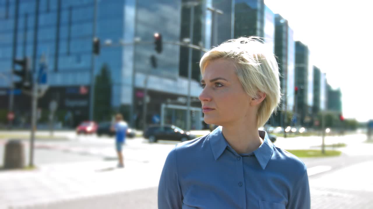 una mujer de negocios seria se encuentra en el centro de la ciudad en el distrito de negocios y mira a la cámara lateral