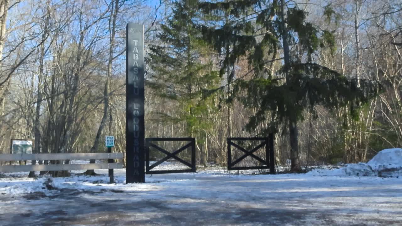 Gorgeous wooden brown fence entrance to a hiking trail in Tabasalu nature trails during a winter beautiful sunny day while white snow is on the ground and tall pine trees and birch bare trees visible.