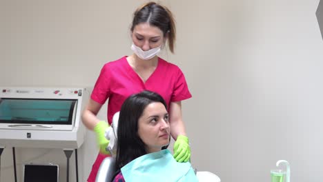 Friendly-female-dentist-putting-on-a-napking-on-young-patient.-Woman-in-dentist's-chair-preparing-to-check-up.-Shot-in-4k
