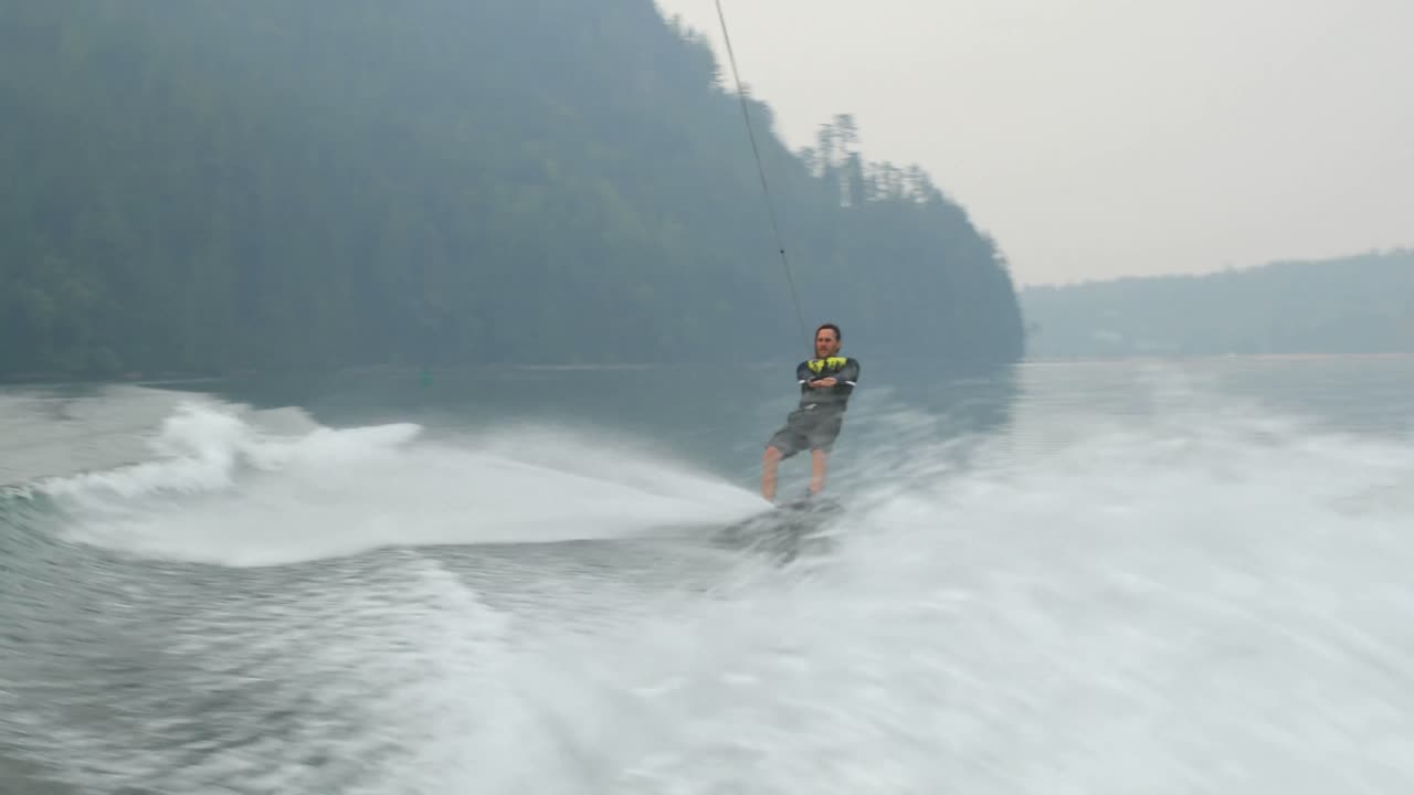 도시 강 4k에서 웨이크 보드에 트릭을하는 백인 젊은이의 앞면