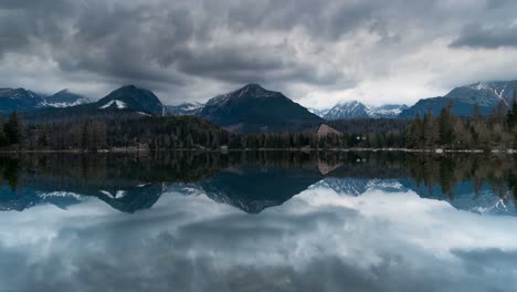 4k wide shot of snowy tatra mountains, calm štrbské pleso lake, pine forest, moody sky, and sunlit trees—perfect for travel, nature, resort, meditation, and landscape footage