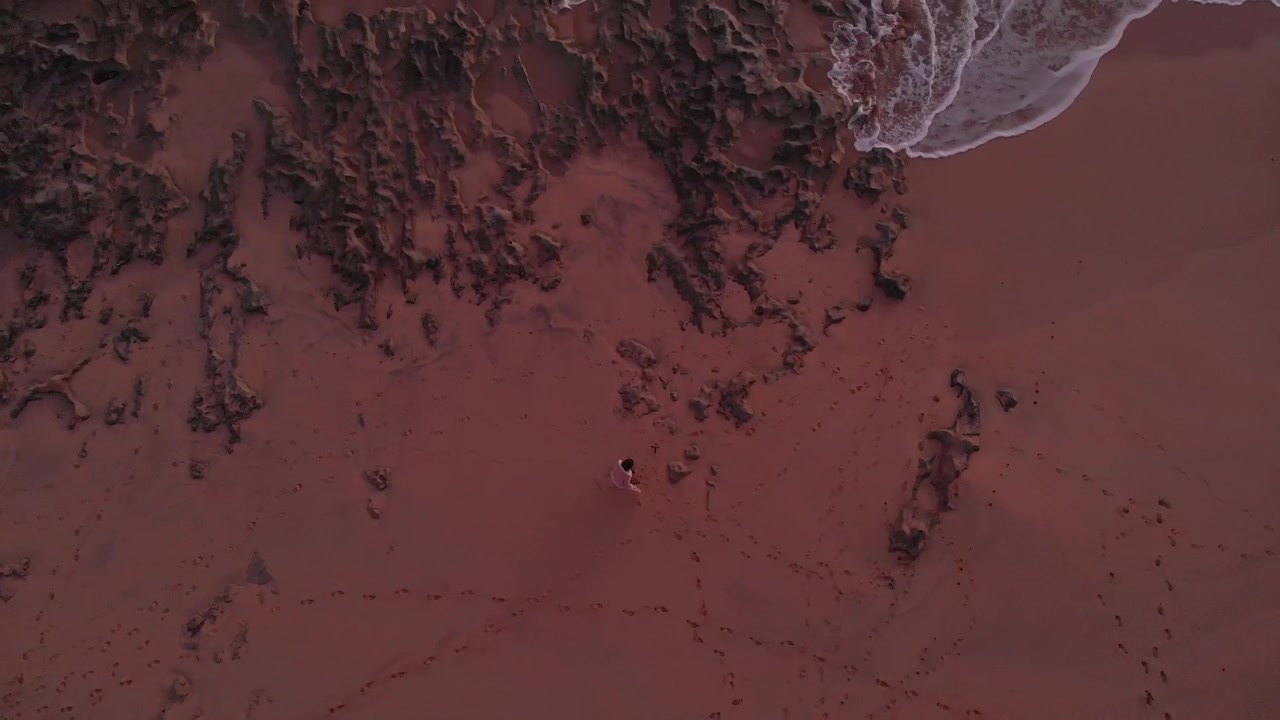 Flyfoto ovenfra av kvinne som vinker på episke solnedgangsfarger på stranden.