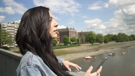 brunette latina tourist taking her phone out and shooting a picture of london from a bridge, slow motion shot