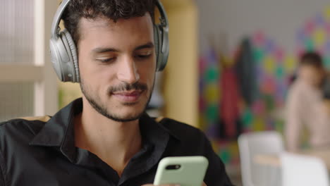 joven hispano atractivo que usa un teléfono inteligente enviando mensajes de texto a las redes sociales estudiante feliz sonriendo navegando en línea escuchando música en una oficina moderna