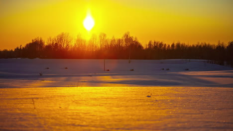 Bright-golden-sun-setting-down-behind-silhouette-of-tree-line-in-winter-season