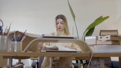 blonde caucasian woman wrapping up piece of clothing and packing for client