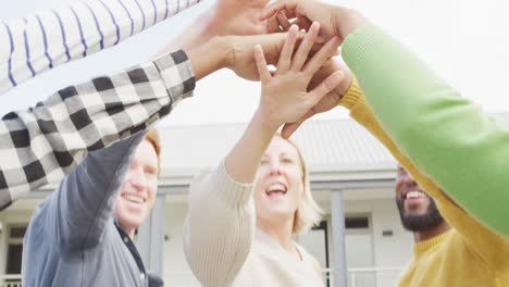 Smiling-diverse-male-and-female-business-colleagues-stacking-hand-and-motivating-in-office