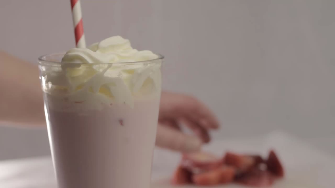 Hand adding fresh strawberries to milkshake close up shot