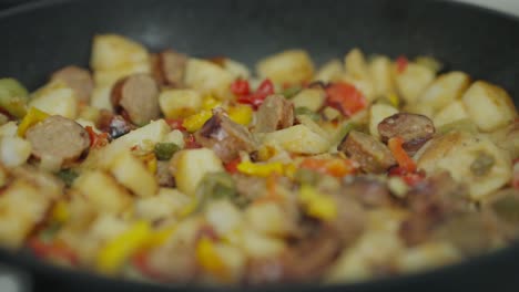 a close-up of sausages, peppers, onions and potatoes being cooked in a cast iron skillet