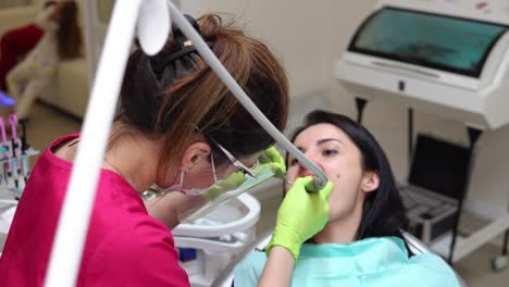 dentist cleans woman's teeth with professional toothpaste and automatic brush. dentist using saliva ejector or dental pump to evacuate saliva.