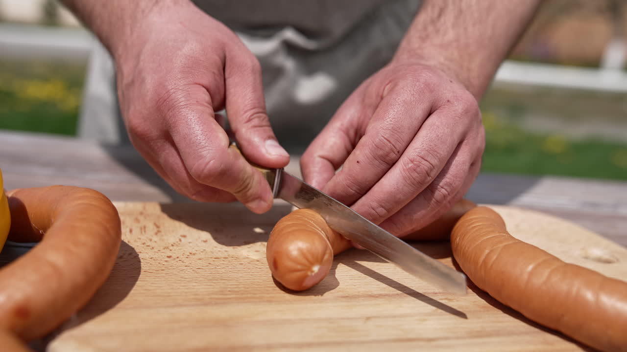 Man's hands cutting sausage to cook on fire. Preparing juicy sausages for barbeque outdoors. Cooking in nature. Close-up.
