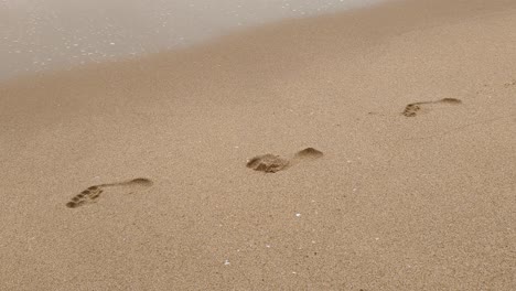 barefoot footprints on sandy beach with frothy waves washing over feet imprints