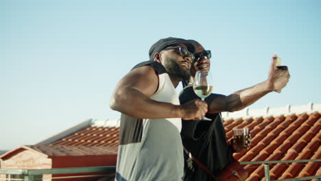 cute gay couple taking selfie with glasses of wine on rooftop