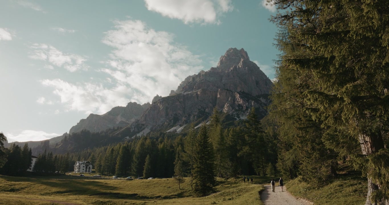 Escursionisti che camminano lungo un sentiero sotto ripide cime rocciose e alberi sempreverdi vicino al Lago di Sorapis nelle Dolomiti, Veneto, Italia. Ampia veduta