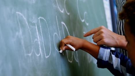 Teacher-assisting-schoolboy-in-writing-alphabet-on-chalkboard