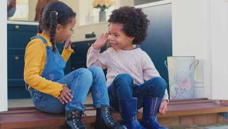 young boy and girl sitting on step at home giving each other high five