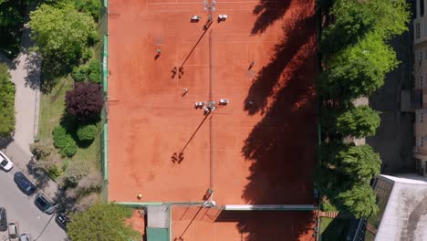 aerial: top down view of clay tennis courts, people playing and sweeping courts