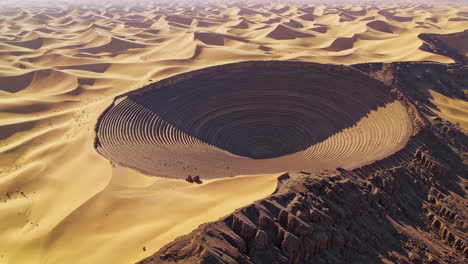 aerial view of a massive terraced circular pit in a vast desert landscape