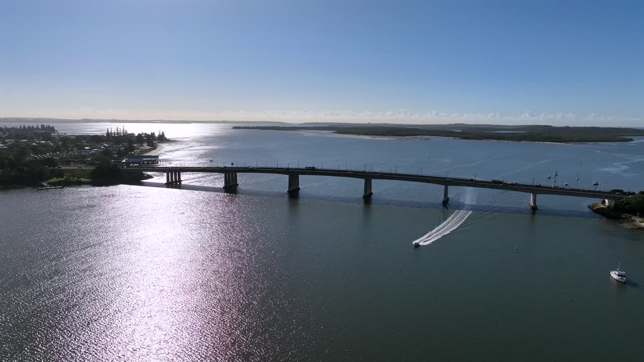 Ampia ripresa aerea con drone di un motoscafo che passa sotto il ponte Captain Cook mentre si dirige a monte da Botany Bay, Sydney.