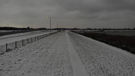 man walks on the middle of the snowy field with fence under overcast