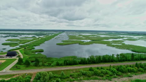 Aerial-of-lake-in-rural-landscape-on-cloudy-day-near-farm-and-green-grass,-Europe