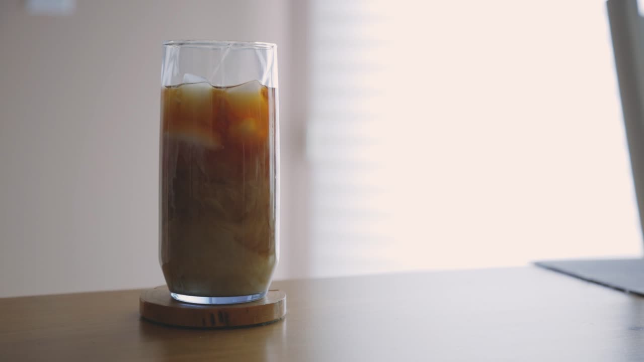 Versando latte fresco in un bicchiere di caffè freddo sul tavolo e mescolare.