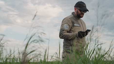 side view of male and female field workers walking through tall grass holding smartphones while surveying open landscape under cloudy sky
