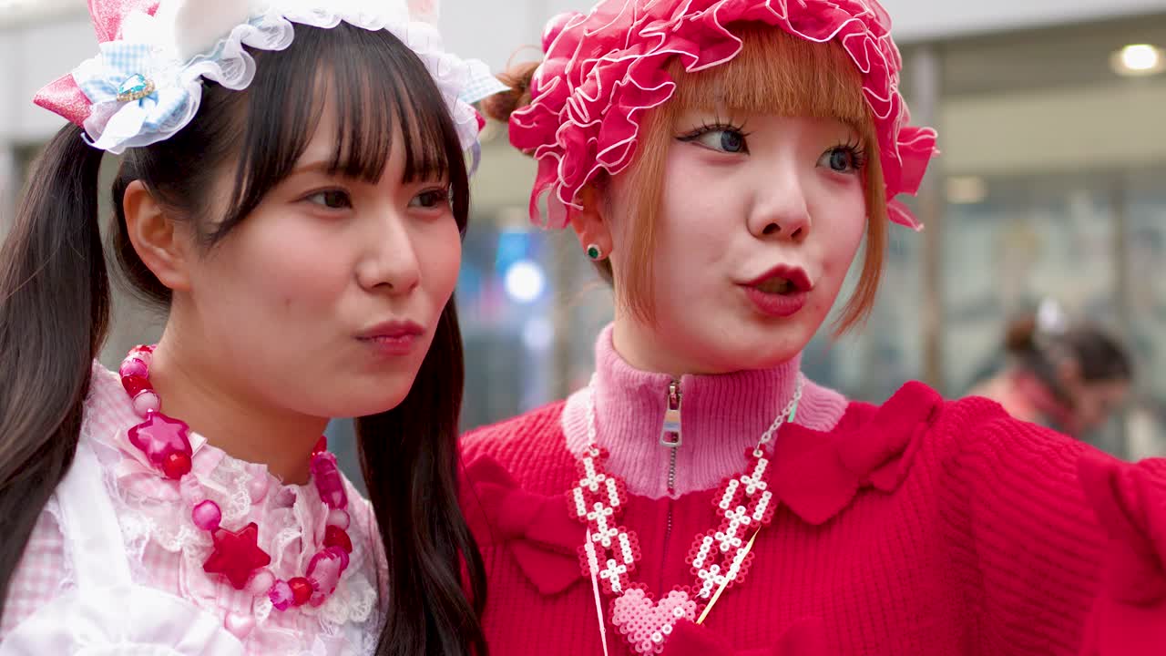 To kvinder i farverig Harajuku gadestil poserer til en selfie på en bygade