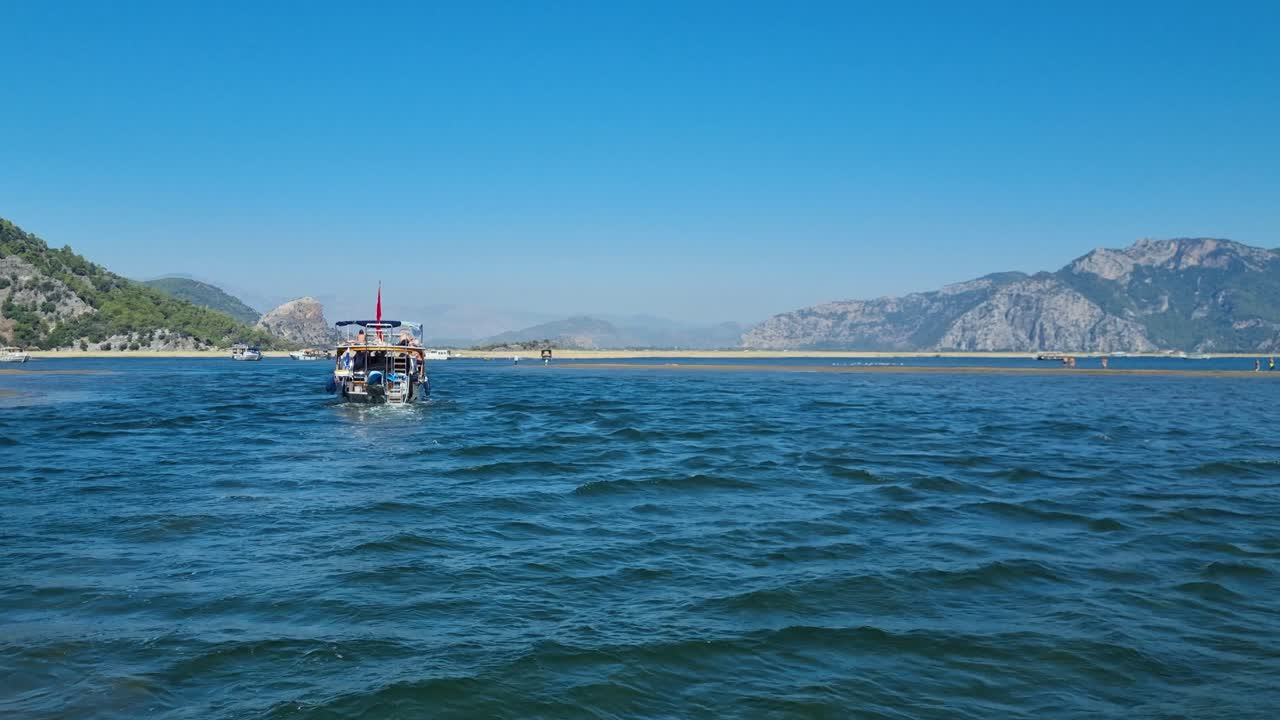 Peaceful boat ride near the Dalyan River delta gliding along the Mediterranean toward Iztuzu Beach, with sandy shores and mountains under clear autumn sun