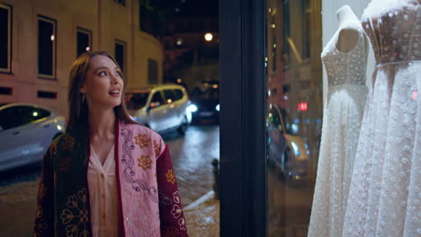 mujer mirando vitrina de boda en la noche ciudad caminar de cerca. niña mirando vestido