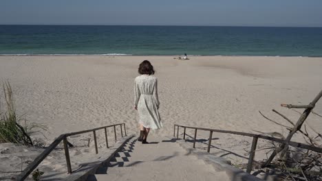 Mädchen-Mit-Dunklem-Haar-In-Weißem-Landhauskleid-Geht-über-Die-Holzleiter-Zum-Meer-Hinunter