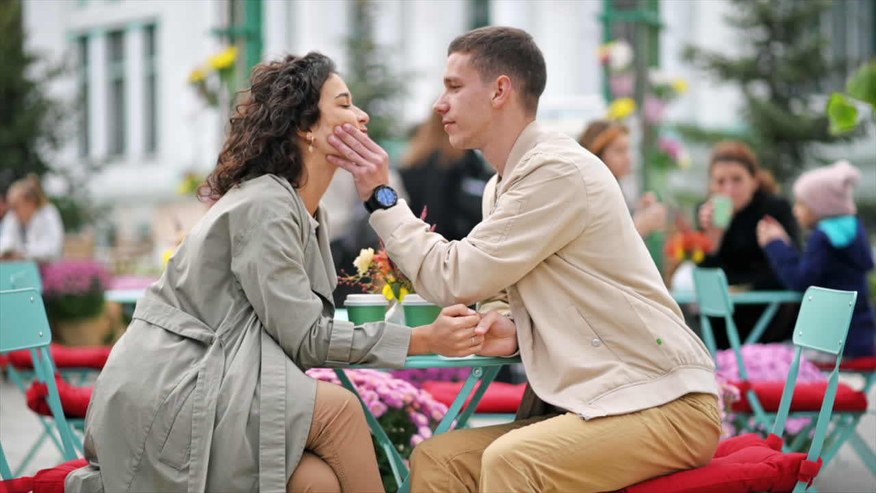 A romantic couple outdoors near a cafe. Holding hands, kissing, flowers on the table. Autumn atmosphere. Slow motion