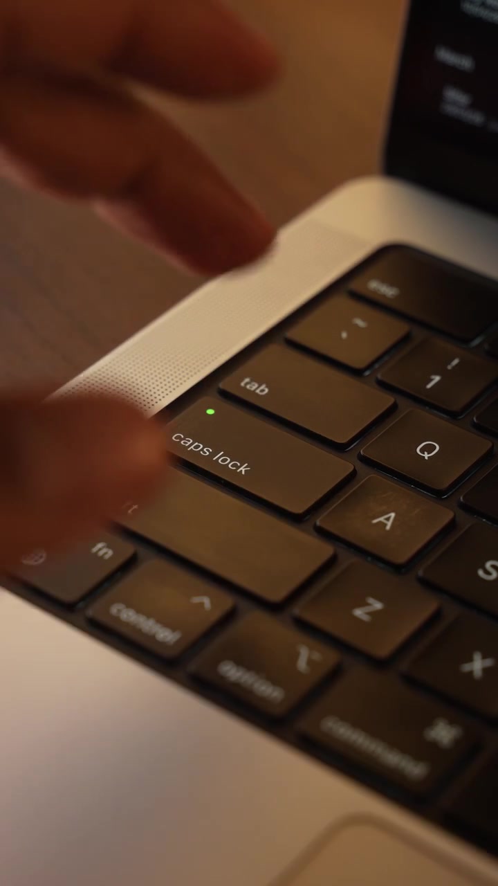 Finger Pressing Caps Lock Button on Laptop Keyboard in Warm Lighted Room.