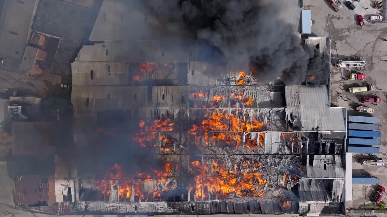 Vista incredibile di un magazzino in fiamme con un'enorme colonna di fumo che si alza.