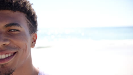 A-young-biracial-man-smiles-with-the-sunlit-beach-as-his-backdrop,-with-copy-space