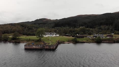 Horses-graze-near-Scotland-flag-waving-from-pier-on-Loch-Ness,-aerial