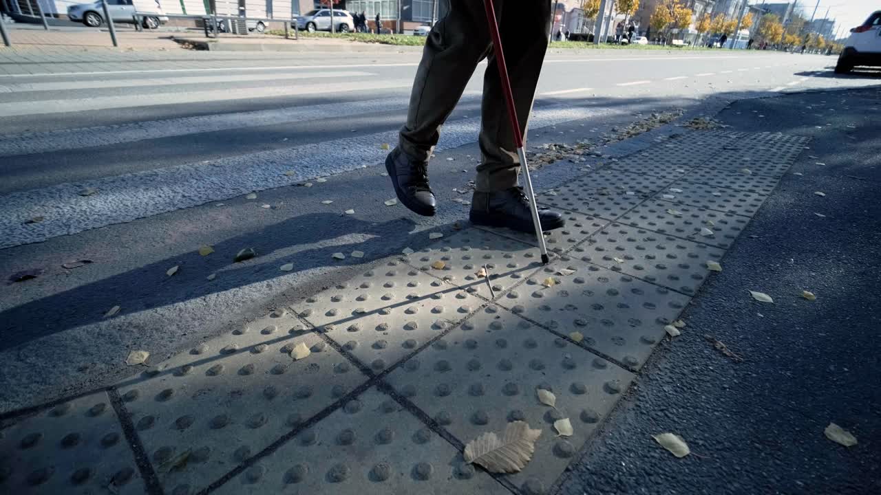 외로운 눈먼 남자가 촉각 타일을 감지하여 보행자가 안전한 도로를 건너고 있습니다.