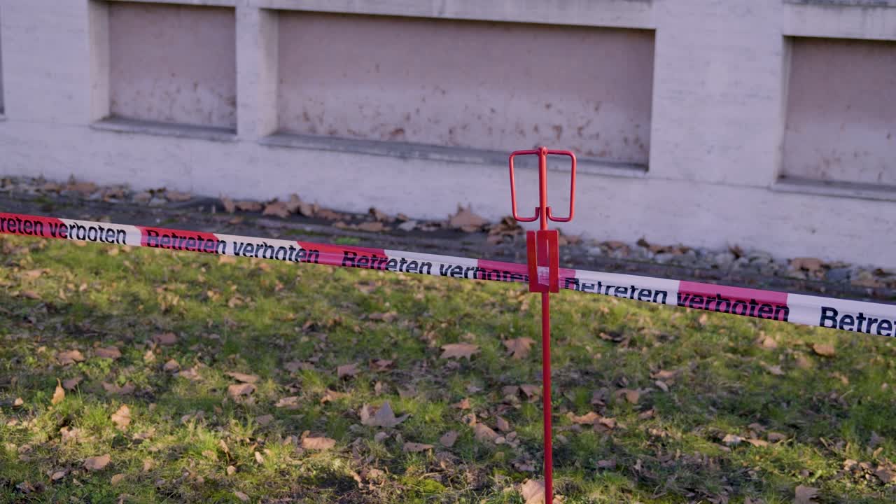 Red warning tape marked "Betreten verboten" around a grassy area near a wall