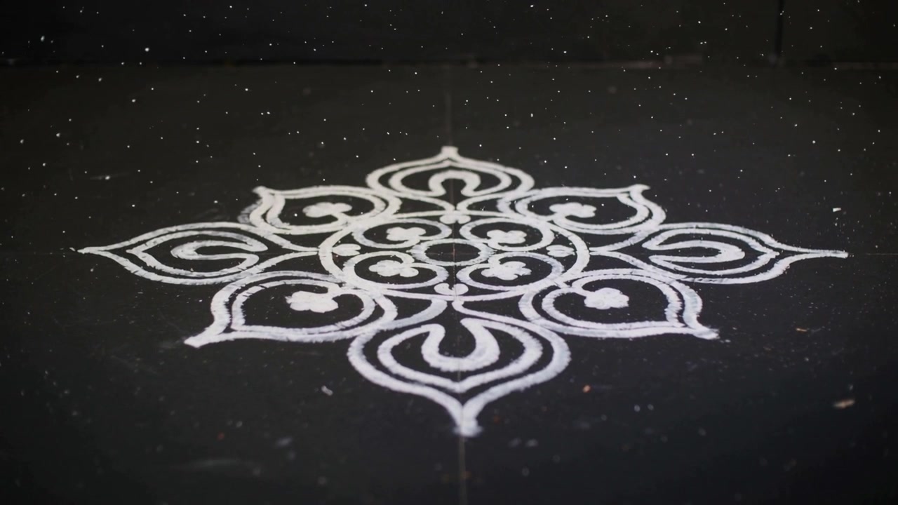 Mostrando un motivo rangoli bianco durante i cambiamenti di messa a fuoco della fotocamera e di luce su una superficie scura con granuli.