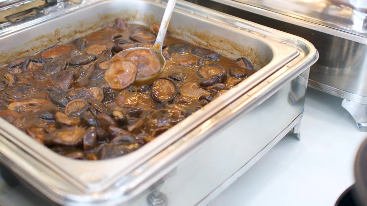 Servire funghi brasati da uno scaldavivande a buffet con tagliatelle verdi.