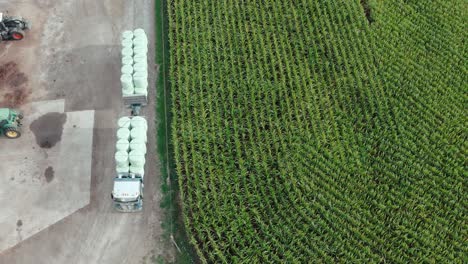 truck transporting round silage fodder bales beside corn field at farm, aerial