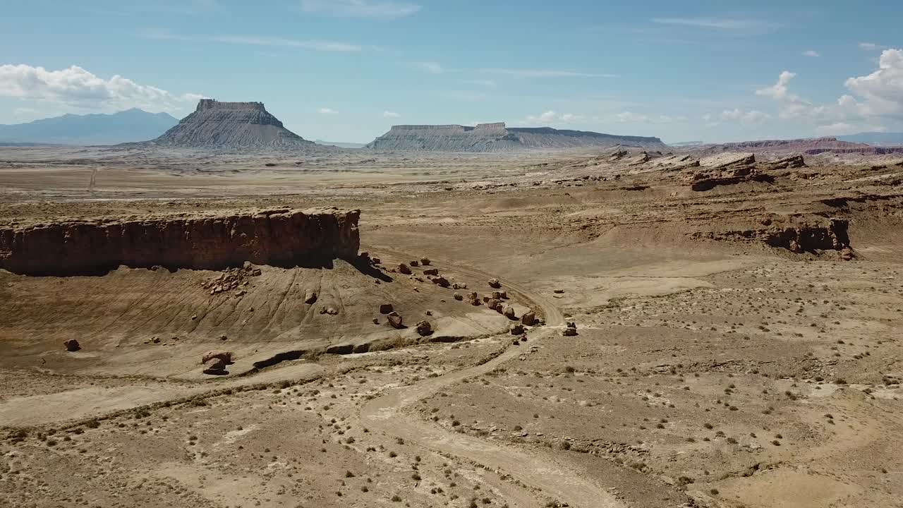 Aerial View of Desert Road Under Rocky Hills in Utah Desert With Factory Butte in Background